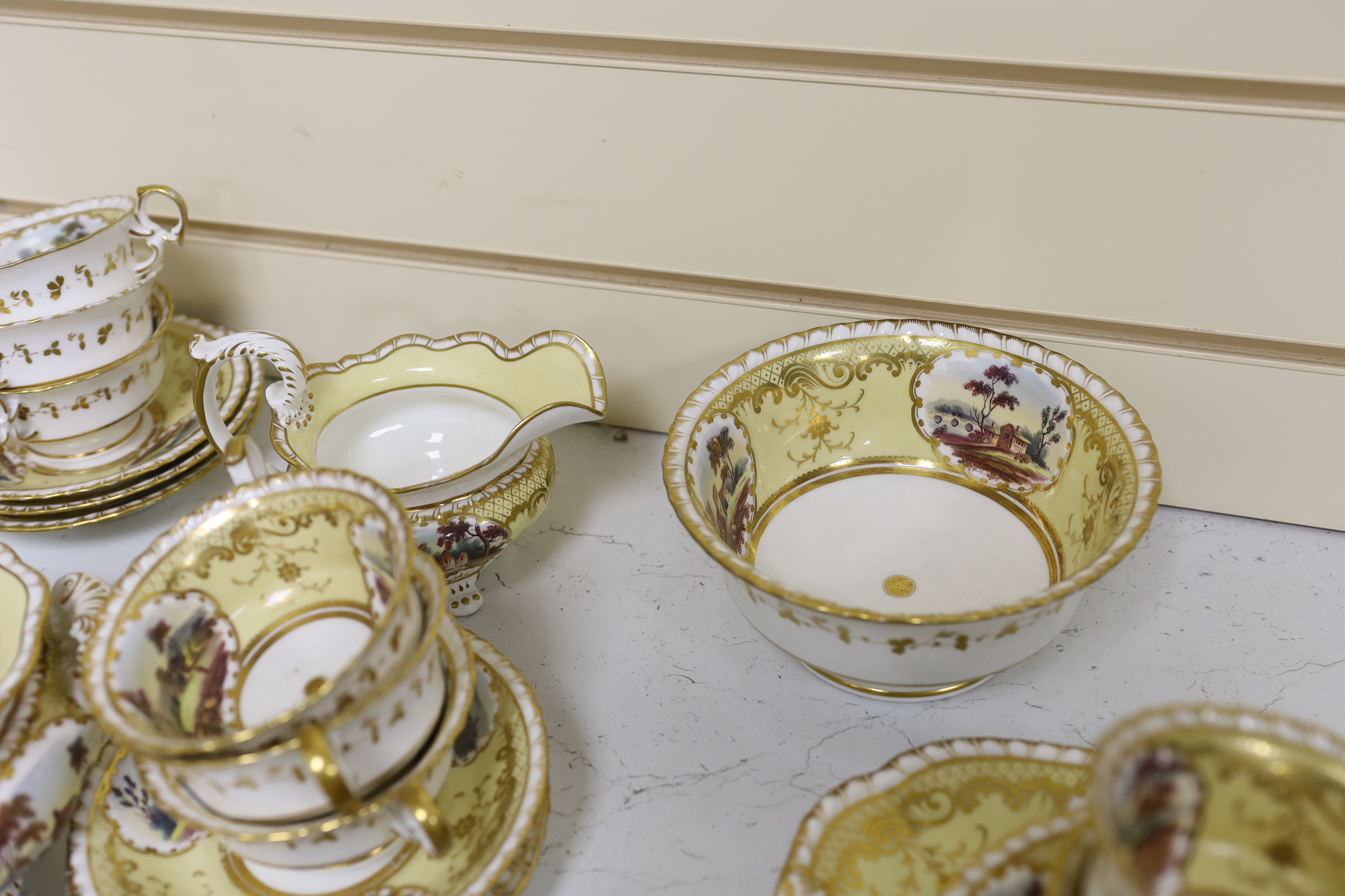 An English porcelain tea set, c.1835-45, including a teapot and cover, sucrier and cover, slops bowl, milk jug, teacups and saucers, two cake plates, each piece painted with buildings in landscapes, yellow ground, patter